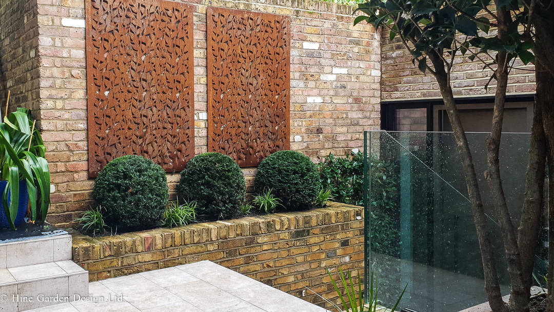 topiary in a london courtyard garden design with corten panels on brick walls with stairs for a level change and glass handrail