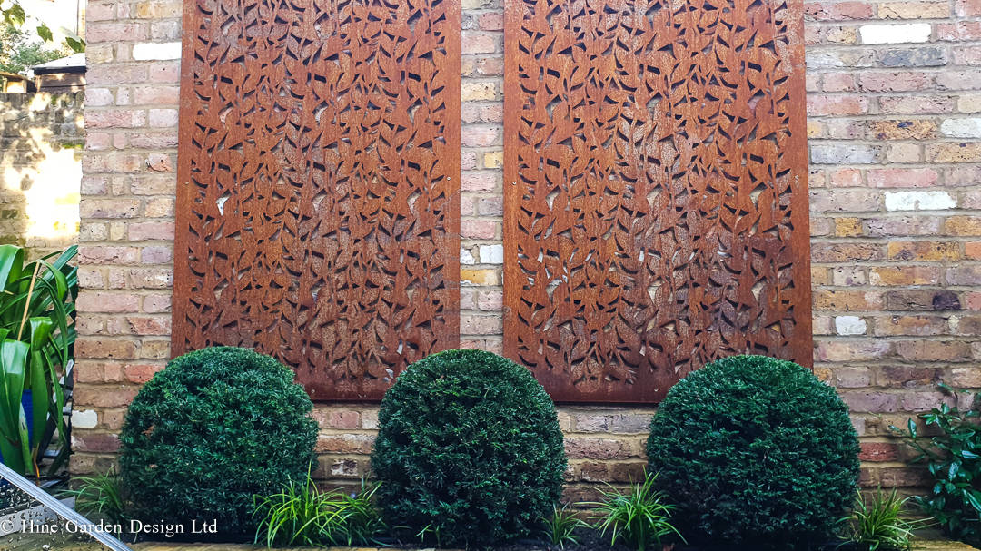 corten panels on a brick wall yew topiary balls in front