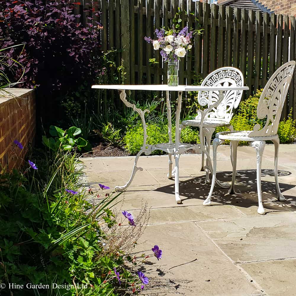 white bistro table on sunlit terrace surrounded bu planting and a low garden brick wall