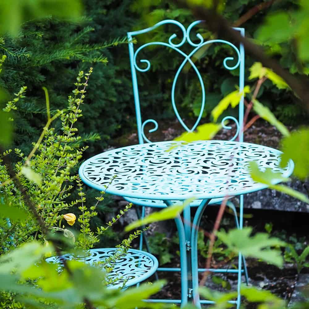 Pale blue garden bistro set surrounded by foliage planting