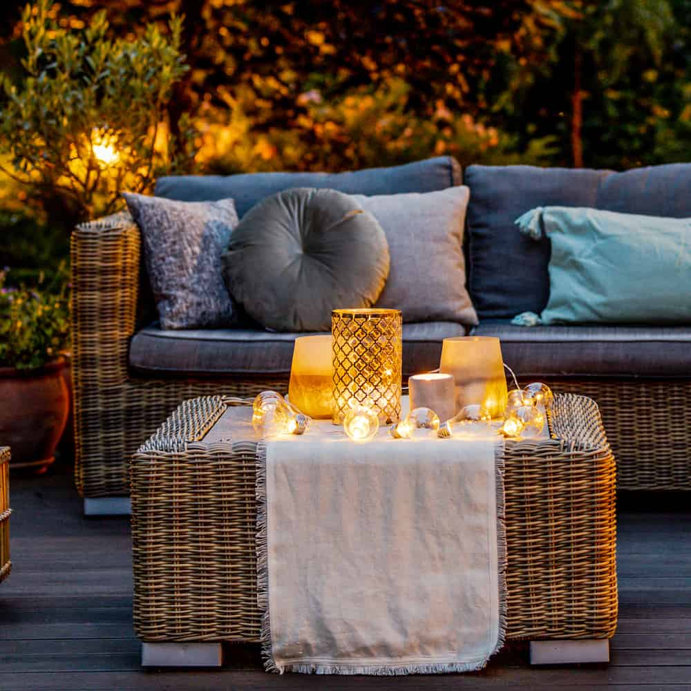 Mid evening day light, the sun fades over comfortable loungs style garden furniture made of rattan, covered in cushions and with matching footstool. Lit mainly with candles for atmosphere.