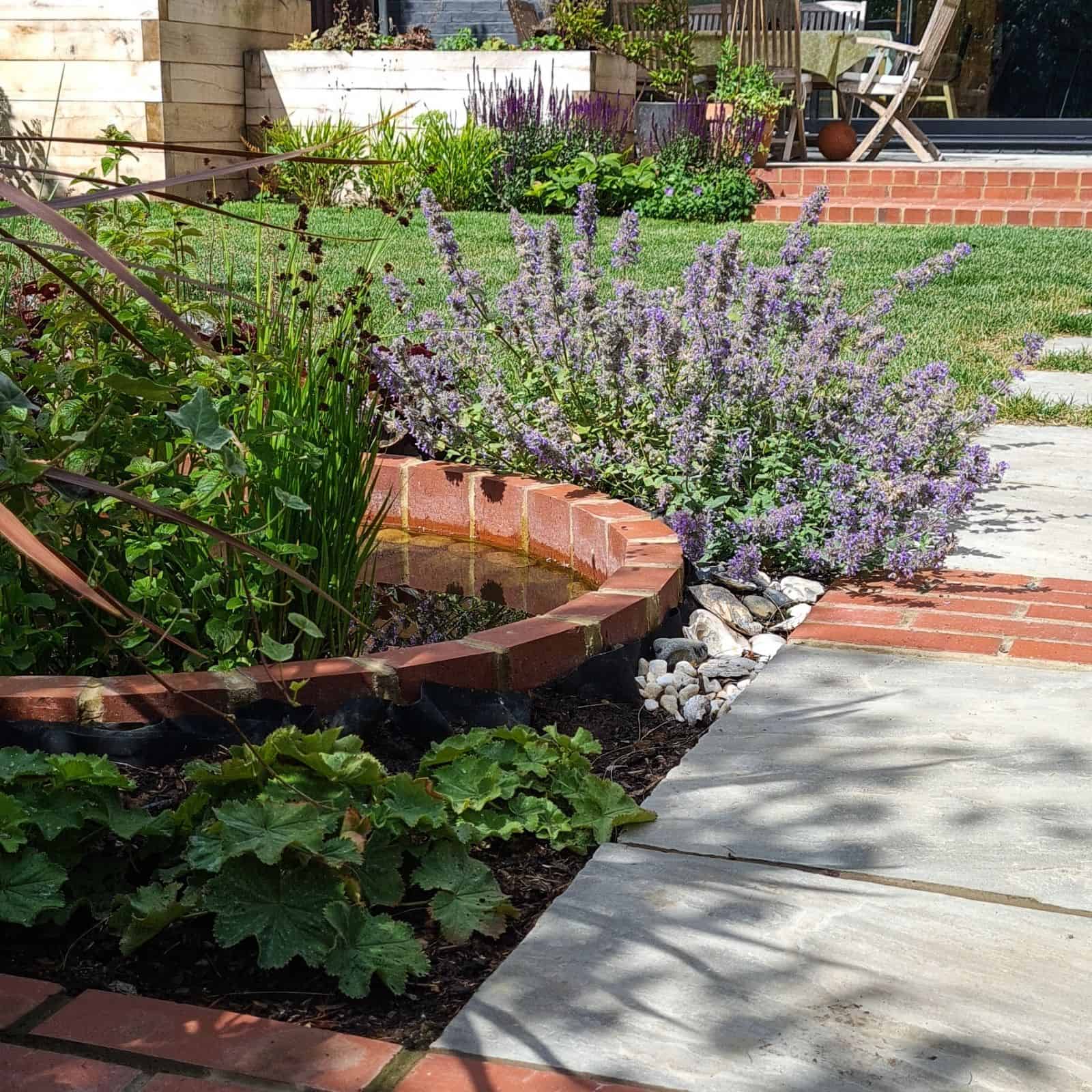 designed steps in garden wall with planting and corner pergola in white surrounding a garden area for entertaining with dining table